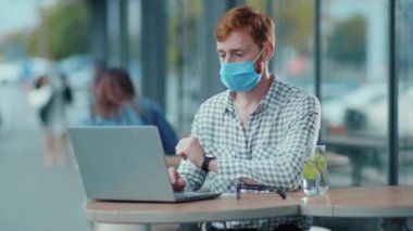 Ginger ofisteki koruyucu solunum maskesi takan ve laptopta çalışıp kafenin terasına serbest proje yazan adam. Yaz. Salgın. Coronavirüs.