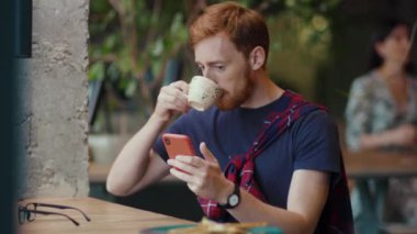 Zencefilli işadamı cep telefonuyla mesajlar yolluyor ve kapalı bir restoranda kahve molası veriyor. İnsanlar ve akıllı telefonlar.