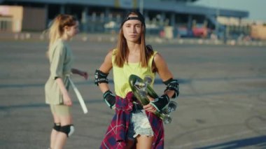 Çekici genç kadın kameraya bak. Elinde kaykayla geziyor. Hippi tarzı sokak tarzı ağır çekim.