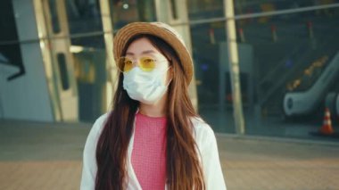 Modern Asyalı kadın gezginin portresi ariport terminalinin yanında duruyor. Koronavirüs hastalığının kilit altına alınması konseptine karşı virüs koruması maskesi takıyor..