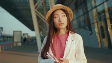 Zarif, güzel Çinli bir kadın, elinde seyahat biletleri ile havaalanı terminalinde mutlu mesut tatilin tadını çıkarıyor. Moda kadın portresi. Asya kökenli. Açık hava..