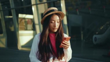 Uçağa bindikten sonra bavulunu havaalanının yanında tutan cep telefonu iletişim cihazıyla genç, hoş bir Çinli kadın. Turist kız. Asya etnik kökeni.