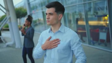 Sağlıksız, Kafkasyalı genç iş adamı sokaklarda öksüren grip virüsü yüzünden acı çekiyor. Arka planda iş adamları ve havaalanı binası var. Salgın. Hava enfeksiyonları.