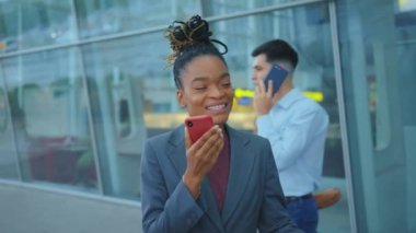 Neşeli Afro-Amerikalı genç bir kadın hoparlörden konuşuyor. Akıllı telefon uygulaması açık havada en iyi arkadaşıyla iletişim kuruyor. Havaalanı binası. Meşgul iş adamları.