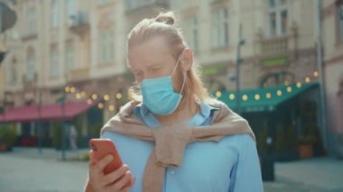 Coronavirus. Salgın. Açık hava portresi çekici kızıl ciddi sakallı iş adamı koruyucu tıbbi maske takan cep telefonu kullanıyor..