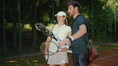 Spor giyim sektöründeki çekici erkek ve kadın raketler ve spor müsabakalarıyla sahada tenis hakkında konuşuyorlar. Genç sporcu bayan sporcu ağır çekim antrenmanı yapıyorlar.