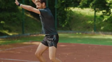 Güneşli bir günde tenis oynayan komik bir genç adam tenis raketi tutuyor. Spor kıyafetleri, spor kıyafetleri, sağlık ekipmanları, yavaş çekimde birbirine uyuyor.