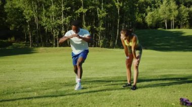 Kişisel eğitmen güzel bir kadın sporcu Afrikalı-Amerikalı bir adamın parkta spor yapmasına yardım ediyor. Açık havada antrenman. Spor çifti.