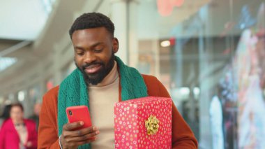 Noel hediyesi olan Afrikalı genç bir Amerikalı 'yı kapatın. Telefonla alışveriş merkezindeki alışveriş merkezindeki internet portresi mobil programcı teknolojisi yavaş çekim hücresine bakın.