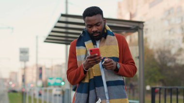 Portre Afro-Amerikalı adam güneşli bir günde şehir merkezinde akıllı telefon standı öksürüğü kullanıyor.