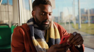 Yüzü gülümseyen Afrikalı Amerikalı genç adam tramvay trafiğinde akıllı telefon kullanıyor. Güneşli bir günde daktilo yazıyor. Yakışıklı yolcular internet mesajlaşmalı portreci çocuk yavaş çekim kullanıyor.