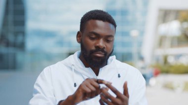 Gülümseyen Afro-Amerikalı adam şehirde fütürist cam telefon yürüyüşü yapıyor. Kameraya bak. Nano-martfon şeffaf elektronik gelecekteki küresel bilgi yenileme arayüzü.
