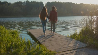 NEW YORK - 5 Nisan 2019: Güzel gölde köprüde el ele yürüyen ve muhteşem manzarada yaz günbatımının tadını çıkaran genç çekici kadın çift. Aşk, ilişki kavramı.