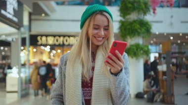 Gülümseyen genç ve çekici bir kadın alışveriş merkezinin portresinde cep telefonu kullanıyor. Gülümsüyor. Yılbaşı hediyesi alıyor.