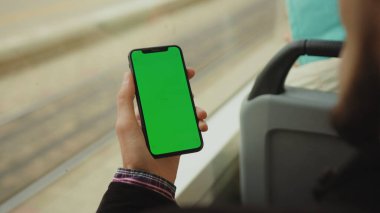 NEW YORK - 19 Mayıs 2019: Genç bir adam, dikey yeşil ekran arka plan tramvayı olan bir cep telefonunu kullanıyor.