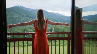 Ağır çekimde ayakta duran ve parmaklıklara yaslanan kadın. Dağların yakınındaki balkonda kaldırılan eller. Turizm, çekici tatil.