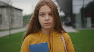 Okul için hazır neşeli genç bir öğrenci elinde okul bahçesinde duran bir sırt çantasıyla. Yeşil bölgede, açık havada gülümseyen güzel bir kızın portresi..