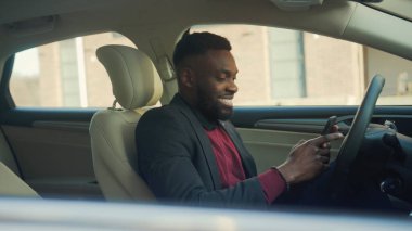 Mutlu afro-amerikan genç işadamı bir arabada telefon kullanıyor gülümsüyor direksiyonda oturuyor genç gülümsüyor araç açık yolcu koltuğu otomobil sokağı otomobil işadamı ceketini yavaş çekimde al