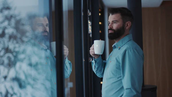 Close up young handsome man bearded drinking coffee and enjoying view from window relax handsome male tea window apartment attractive caucasian human face relaxation adult panorama indoors slow motion