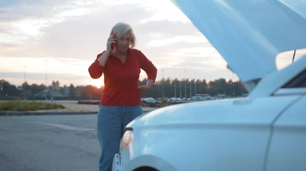 Close up senior businesswoman speak on phone stand near opening the hood broken down car driver sunset road service emergency travel woman auto breakdown call down nature slow motion