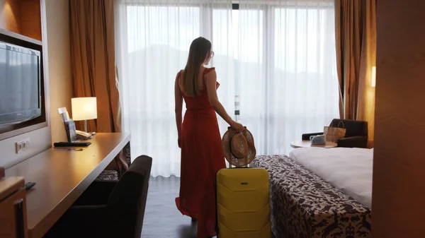 Close up shot back young woman is entering opening curtain lace standing in luxury apartment alone rolling her suitcase and inspecting space feel happy apartment tourist trip holiday slow motion