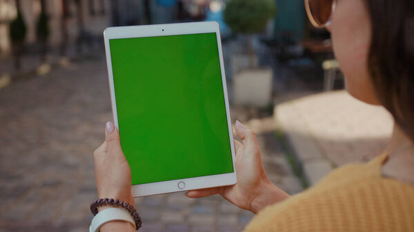 Боковой крупный план общительной женщины, держащей планшетный компьютер с пустым зеленым макетом дисплея, стоящим в центре города. Люди и современные технологии.