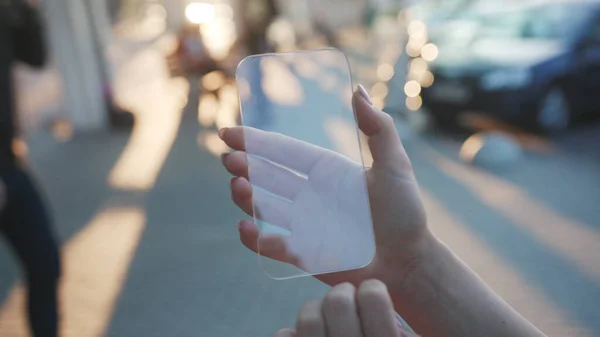 Woman hand with transparent virtual smartphone on blurred street background. Close-up young swiping tapping on holographic screen for animation staying in the city center.