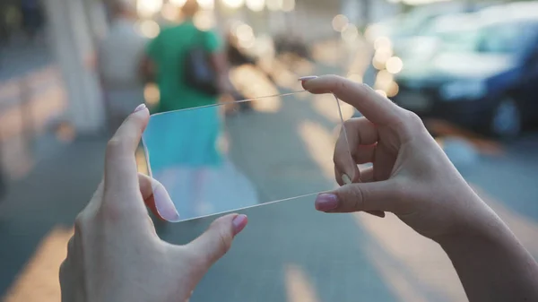 Woman hand with transparent virtual smartphone on blurred street background. Close-up young swiping tapping on holographic screen for animation staying in the city center.