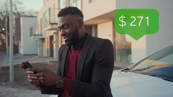 App Icon with Online Transaction. Financial Transactions in the Smartphone. Receive a Message About Increase Money. Happy African American Young Businessman Use Phone In A Car Smile Sits Behind The