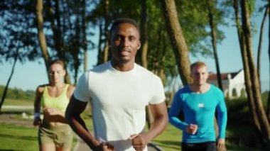 Bir grup iyi eğitimli sporcu ve sporcu güzel yaz manzarasında parkta tek başlarına koşuyorlar. Açık hava eğitimi. Fitness insanları. Egzersiz.