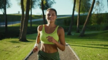 Güzel, genç, zayıf ve kaslı formalı, parlak sarı spor giysili kız sabahın erken saatlerinde parkta koşuyor. Sporcu kadın. Aktif ve sağlıklı yaşam tarzı.