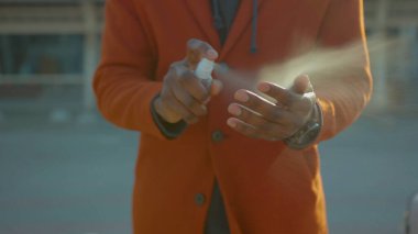 Günbatımında, Afrika kökenli Amerikalı erkek, temizlik için el dezenfektanı spreyine serpiştirir ve havaalanındaki COVID-19 Coronavirus enfeksiyonunu önler.