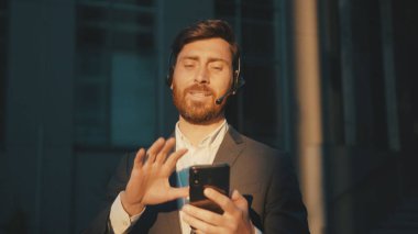 Gün ışığında şehir merkezinde yürüyen mutlu genç adam telefon ve kulaklık kullanır. Mesajlaşır, güler yüzlü, güler yüzlü, iletişim kurar. Gün ışığında yavaş çekim başarılı olur.