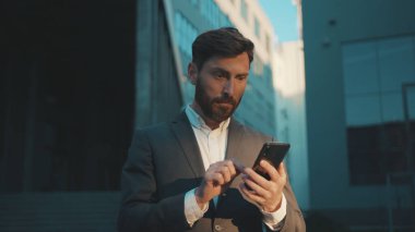 Şehir merkezindeki iş adamı durağında çekim yapmak için telefon mesajlaşması, kaydırma, güler yüzlü gülümseme teknolojisi, güneşli gün başarısı, ağır çekim.