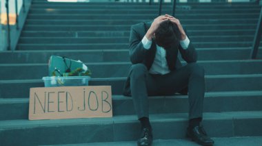 Merdivenlerde elinde kişisel eşyalar ve yazılı posterle oturan hayal kırıklığına uğramış genç adam Coronavirus krizi yüzünden işten atıldı.