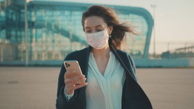 Neşeli genç iş kadını akıllı telefondan salgın haberlerini kontrol ediyor. Karantinanın sona ermesini kutlayan tıbbi maskeyi çıkarıyor. Coronavirus kazandı. Sağlık hizmetleri. Yeni hayat.