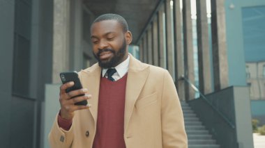 Yüzünüzü kapatın. Ciddi Afro-Amerikalı genç adam telefon kullanıyor. Gün batımında caddede duruyor.