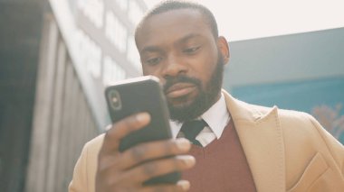 Yüzünüzü kapatın. Ciddi Afro-Amerikalı genç adam telefon kullanıyor. Gün batımında caddede duruyor.