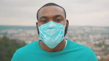2020 Salgını. Koruyucu yüz maskesi takan ve gözlük takan Afrikalı sağlıklı bir adamın portresi şehrin tepesinde dikiliyor. Karantinaya alın. Güvenlik bakımı.