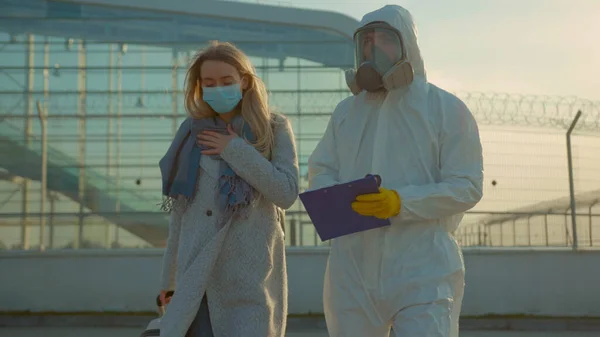 Sick woman with medical worker in protective suit screening passenger walk Covid-19 symptoms coronavirus checkpoints airports mask infection epidemic corona passengers slow motion
