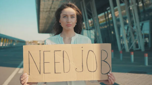 In need of job. Young unhappy woman holding a job search banner hoping for employment striking outside business building. Demonstration. Unemployment, crisis 2020.