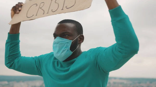 Angry strong african unemployed man fighting against job loss showing Coronavirus Crisis banner shouting call outs on mountain top. Pandemic. Glonal unemployment.