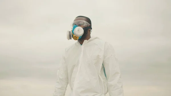 African american young man in chemical protection suit wearing face respirator mask standing on mountain top. Ecology disaster. Save the environment. Pandemic. Coronavirus.