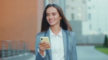 Genç iş kadını telefon yürüyüşü yapıyor. İş merkezi kıyafetinin yakınına bak. Başarılı bir teknoloji gibi görünüyor.