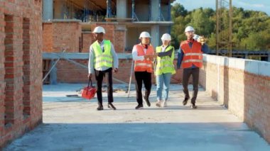 Çok ırklı bir ekip, inşaat alanındaki güneş ışığından geçerek şehir merkezinde gökdelen inşaatçısı mimar müteahhit müteahhit miğferle ağır çekimde miğferle buluşuyor.