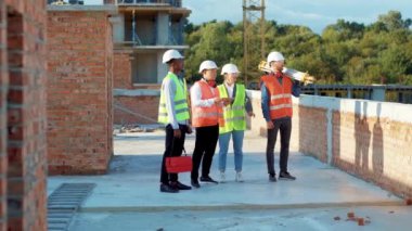 Çok ırklı bir ekip, güneş ışığı, şehir, gökdelen inşaatçısıyla müteahhit müteahhit mimar, mimar, miğferle ağır çekimde miğfer inşaatında ayakta duruyor.