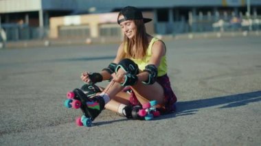 Genç bir kadın yerde oturuyor ve patenleri yerleştiriyor gülümsüyor. Yaz aylarında mutlu bir cadde. Ayaklar patenle kayıyor.