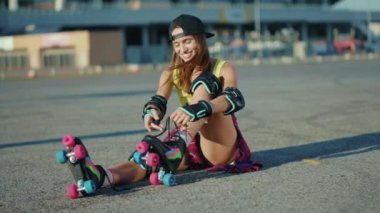 Mutlu genç bir kadın yerde oturuyor ve patenleri yerleştiriyor yazın gülümseyen caddelerde bacaklar patenle kayıyor ağır çekim.