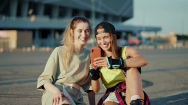 Patenlerle yerde oturan mutlu genç kadınlar yaz aylarında telefonla konuşur güler yüzlü caddelerde bacaklar ağır çekimde patenle kayar.