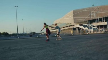 Gün batımında genç güzel kızlar dışarıda paten kayıyor. Eğlenceli sokak bacakları takılıyor. Arkadaşlar patenle kayıyorlar.